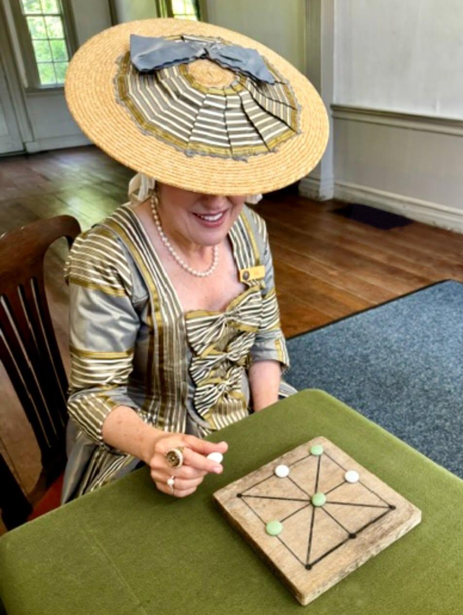 Woman in colonial costume plays historic board game.