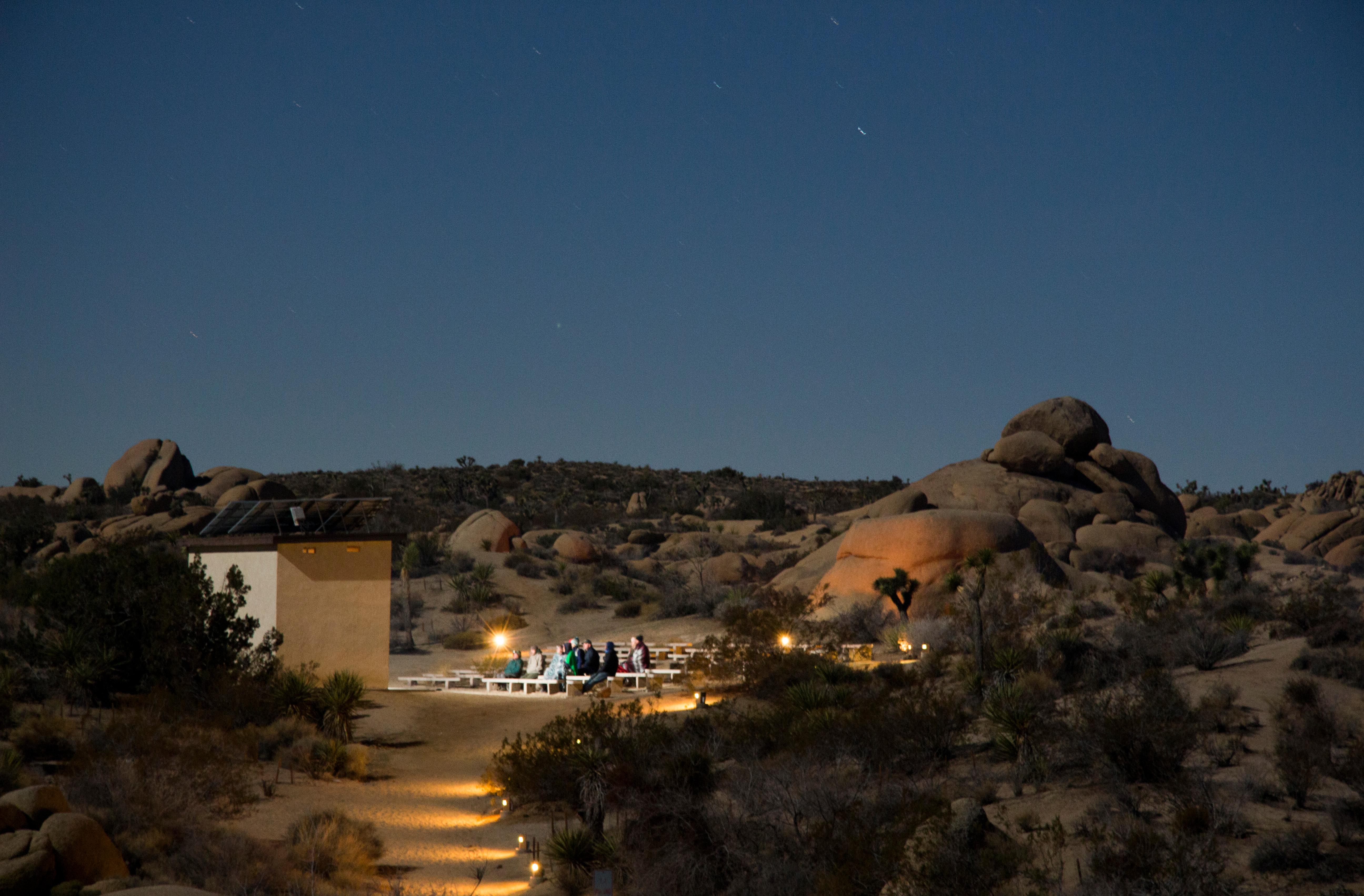Jumbo Rocks Amphitheater at night. There are lights along the path and at the amphitheater.