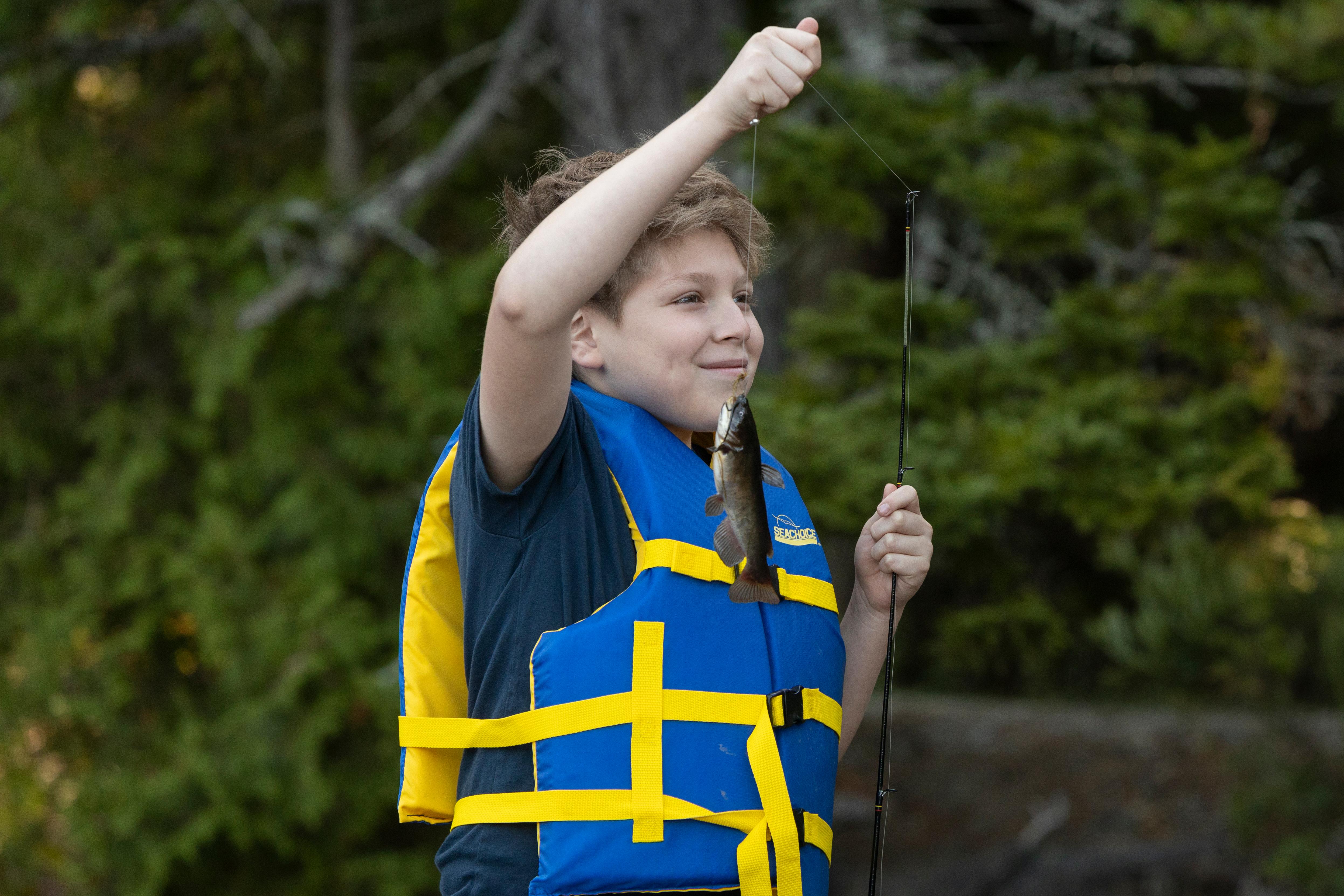 Boy in blue life jacket holding up a small fish