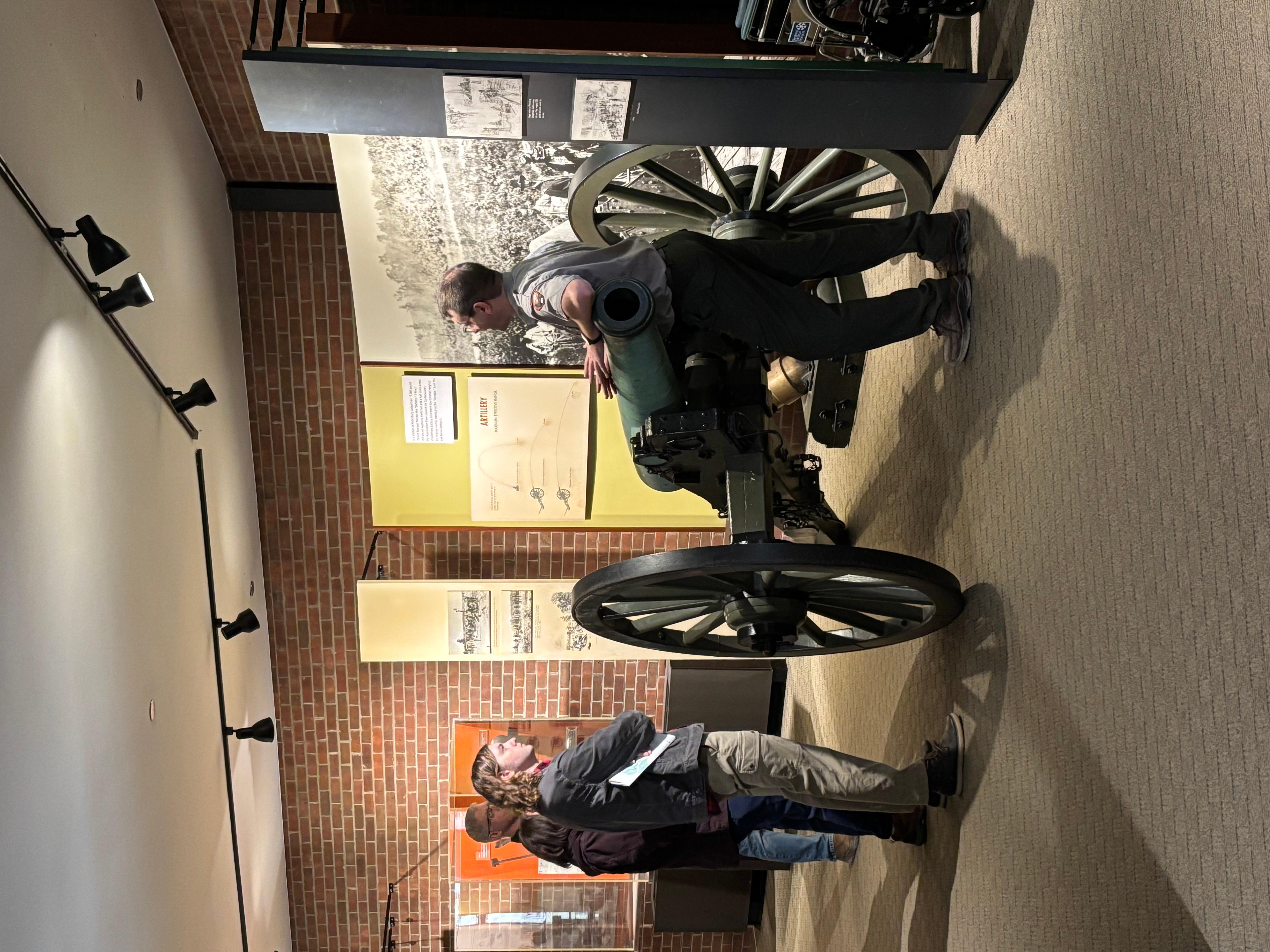 Park Ranger standing next to a cannon talking to visitors inside the Eastern Front Visitor Center