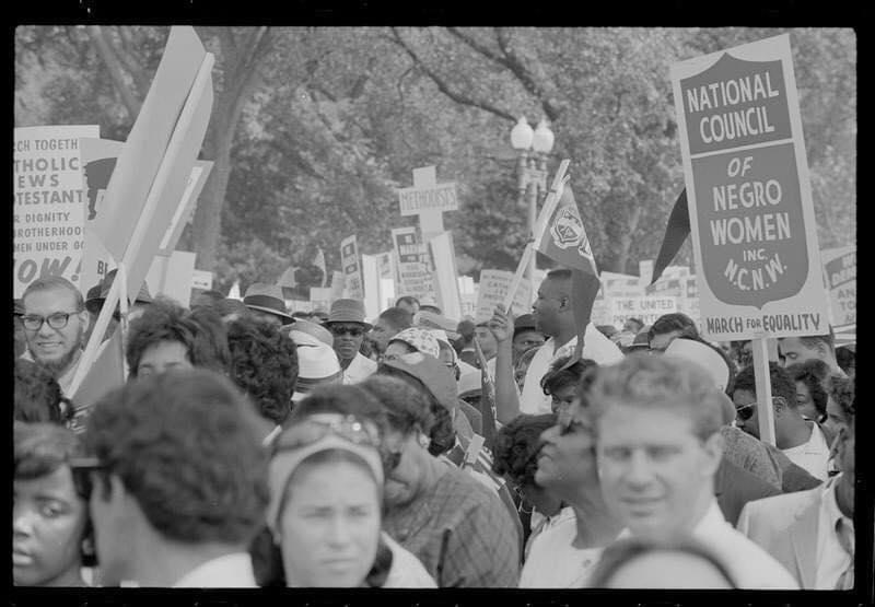Men and women outside holding protest signs with trees in the background