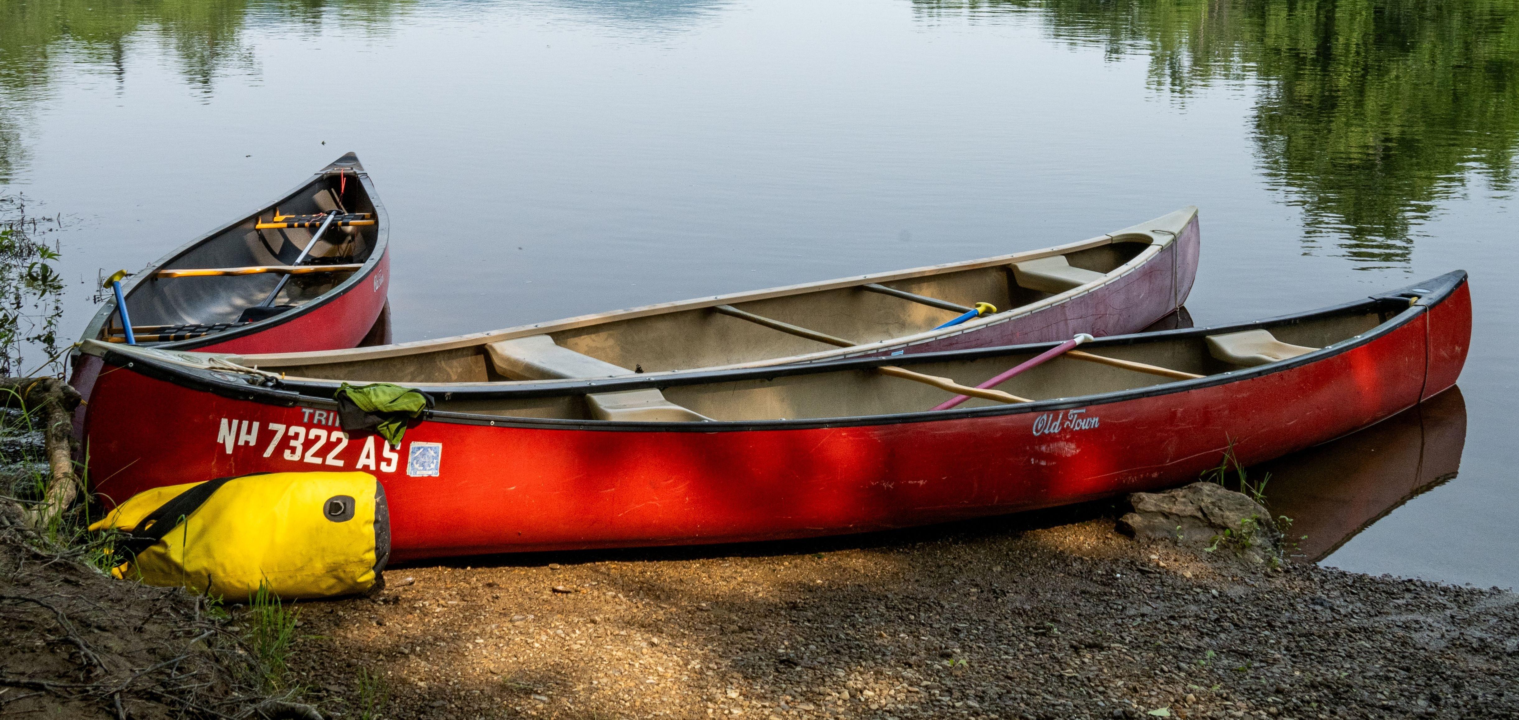 Three red canoes sit on the shore of a calm river.
