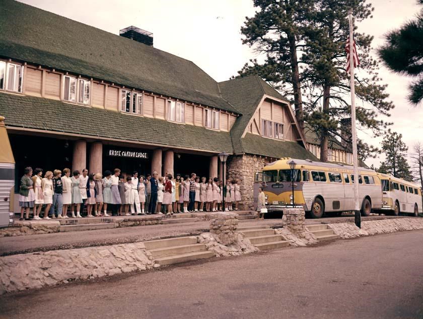 A group of people gather in front of a large lodge with buses lined up alongside