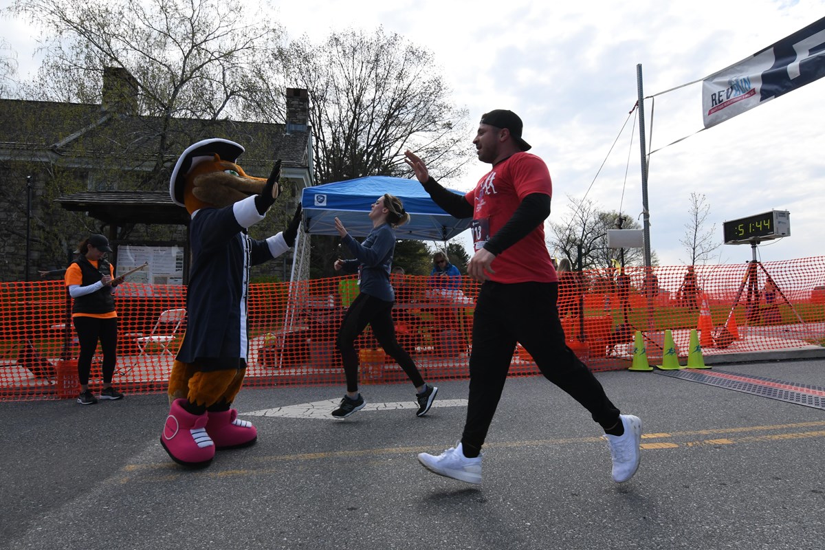 two runners high five a costumed character at the race finish line