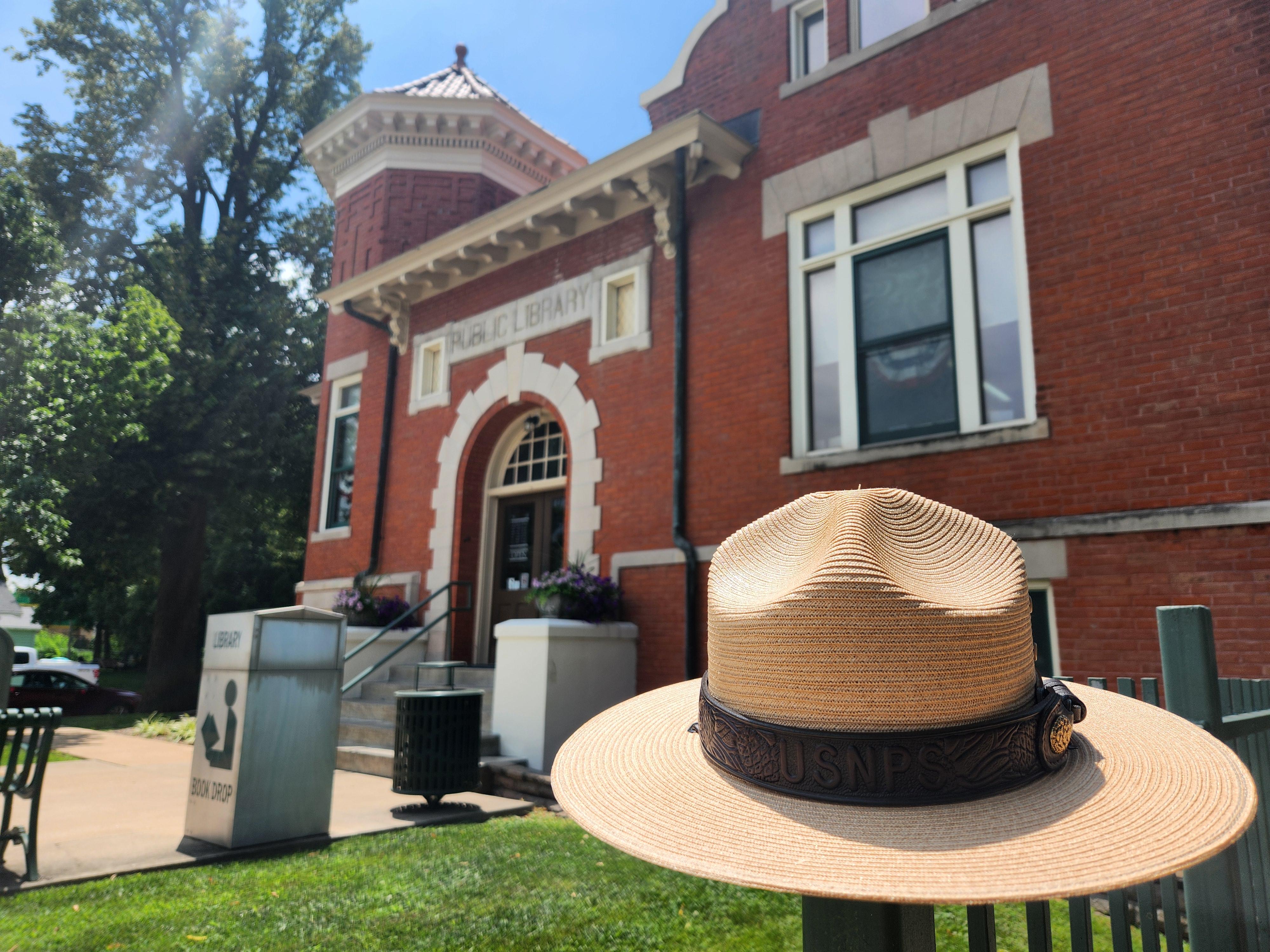 A ranger hat sits on a railing in front of a red-brick building with tall tower.