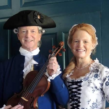 A man in a white wig and black cocked hat holds a violin. He and a woman smile at you.
