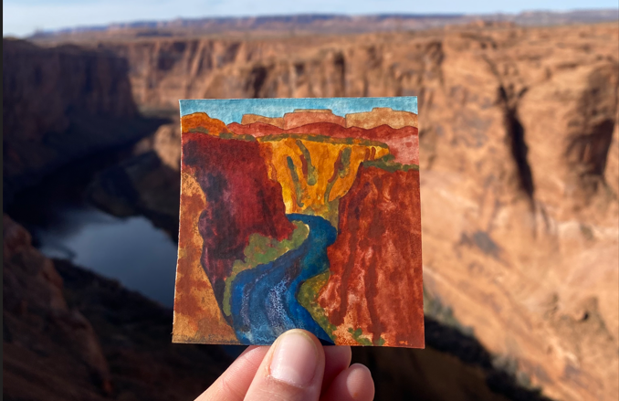 A watercolor painting of a river flowing through a desert canyon being held up to the landscape.