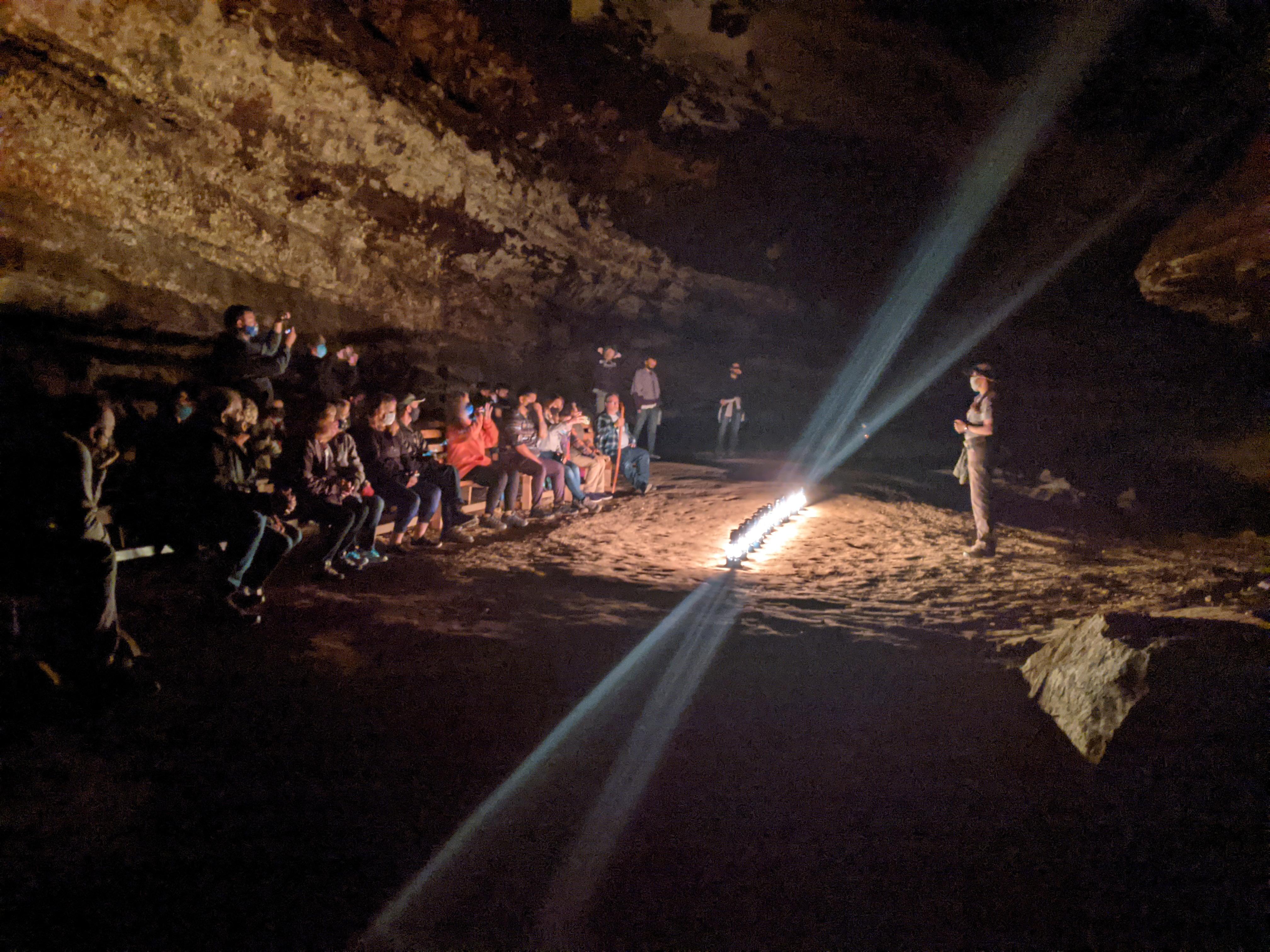 An NPS guide addresses a group in a cave passageway illuminated by lanterns.
