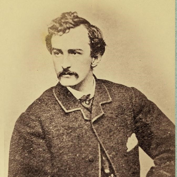 John Wilkes Booth, half-length portrait, facing left and holding a cane.