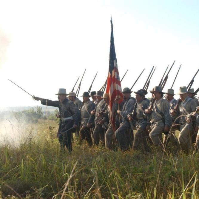 Soldiers in Civil War-era uniforms marching through a cornfield during a reenactment.