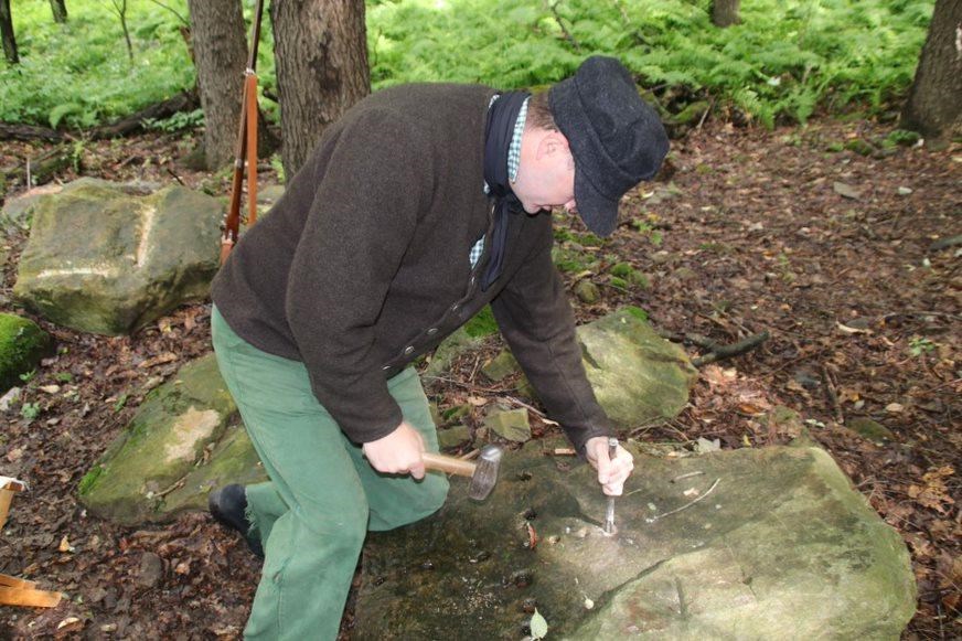 A costumed park ranger performing a stone cutting demonstration