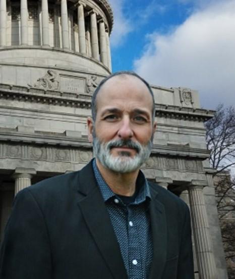 man with gray beard in front of stone classical building