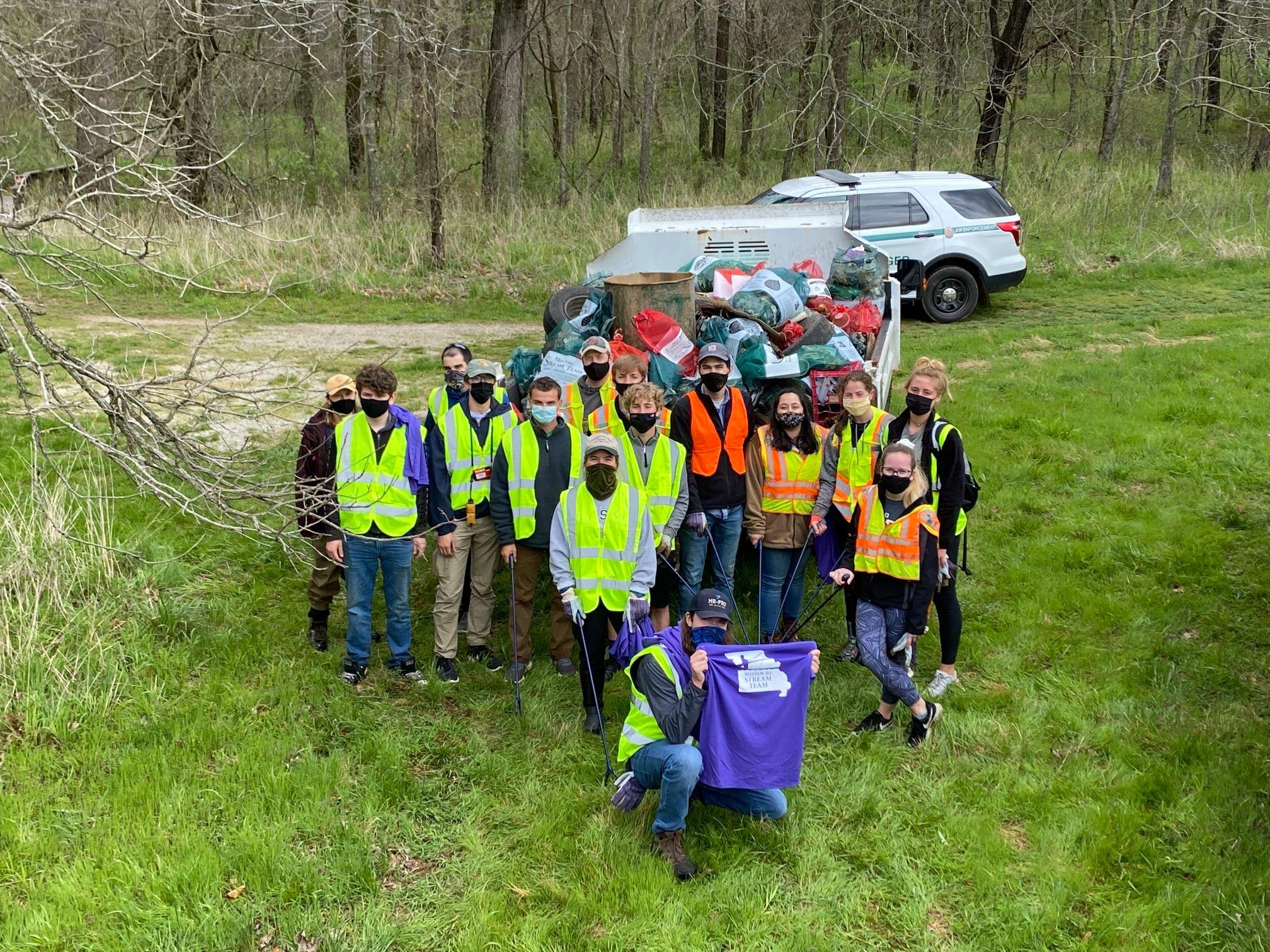 People in reflective vests posing in front of a utility truck filled with bags of trash.
