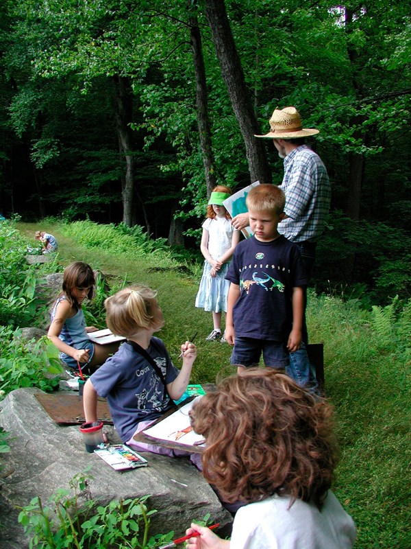 A group of children sitting on rocks and grass creating art.