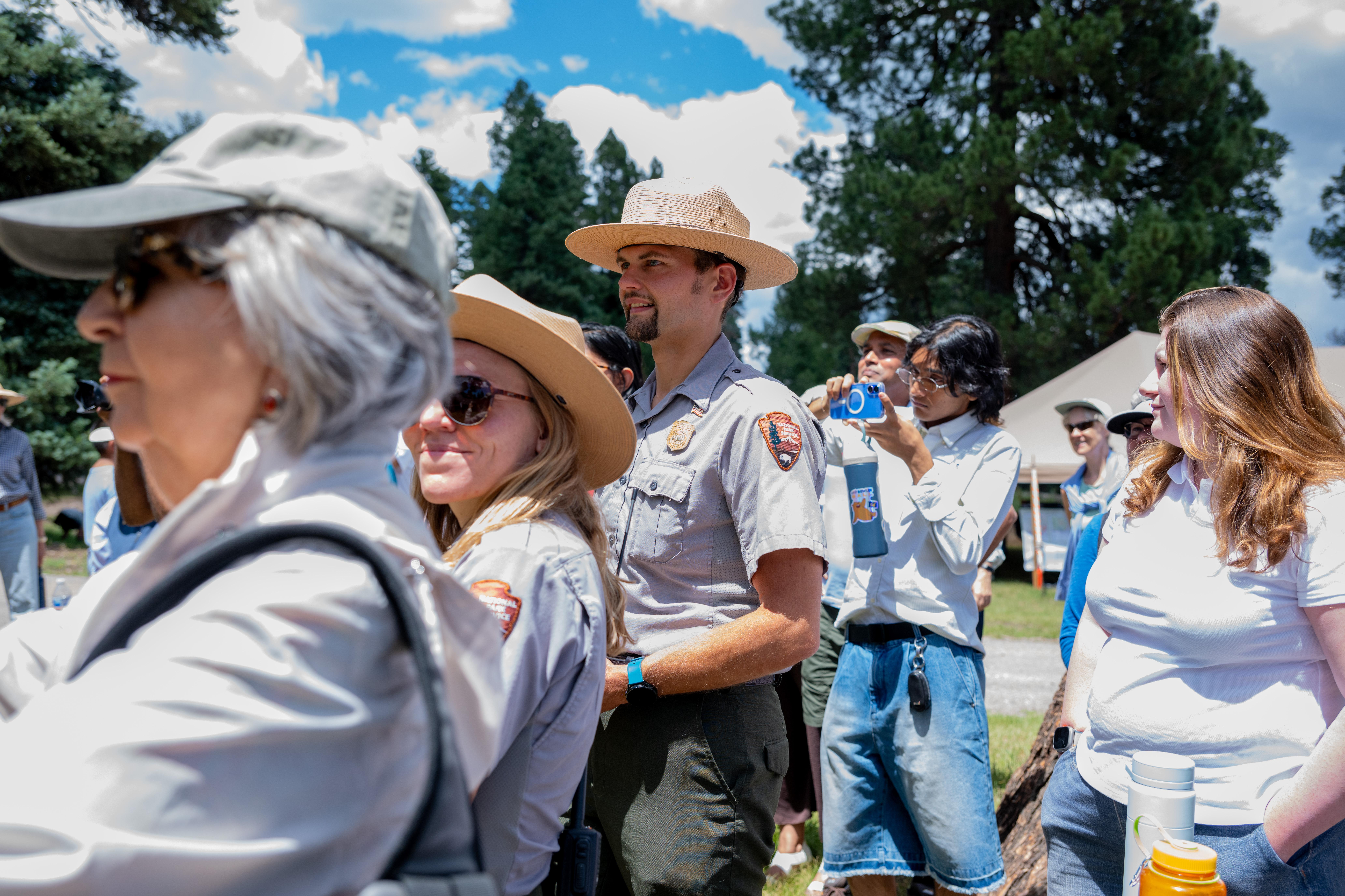 A National Park ranger stands outdoors in a crowd of people.