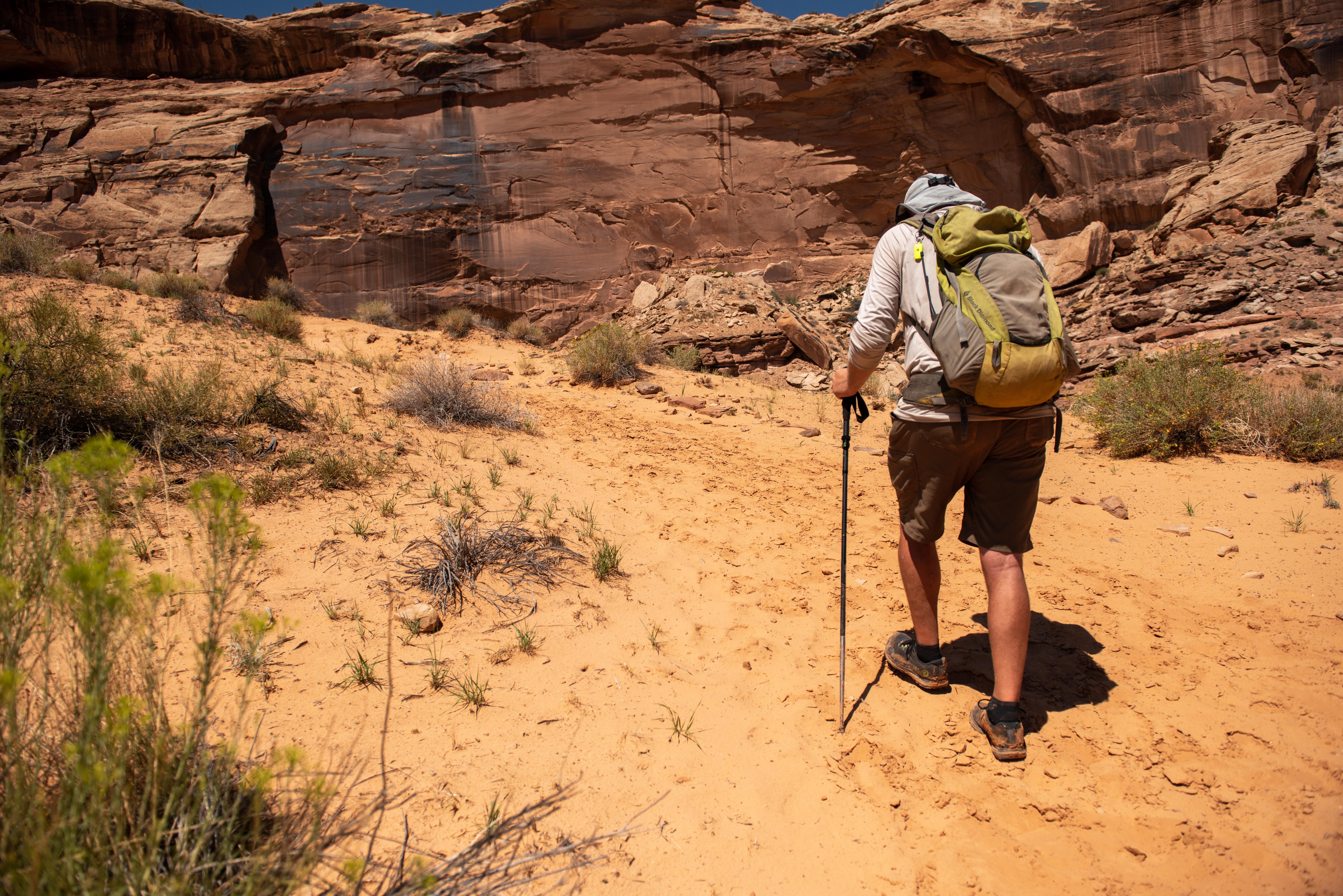 hiker climbs sandy slope near red rock cliff