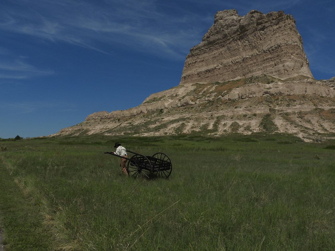 A man pulls a large, wooden, two-wheeled cart.