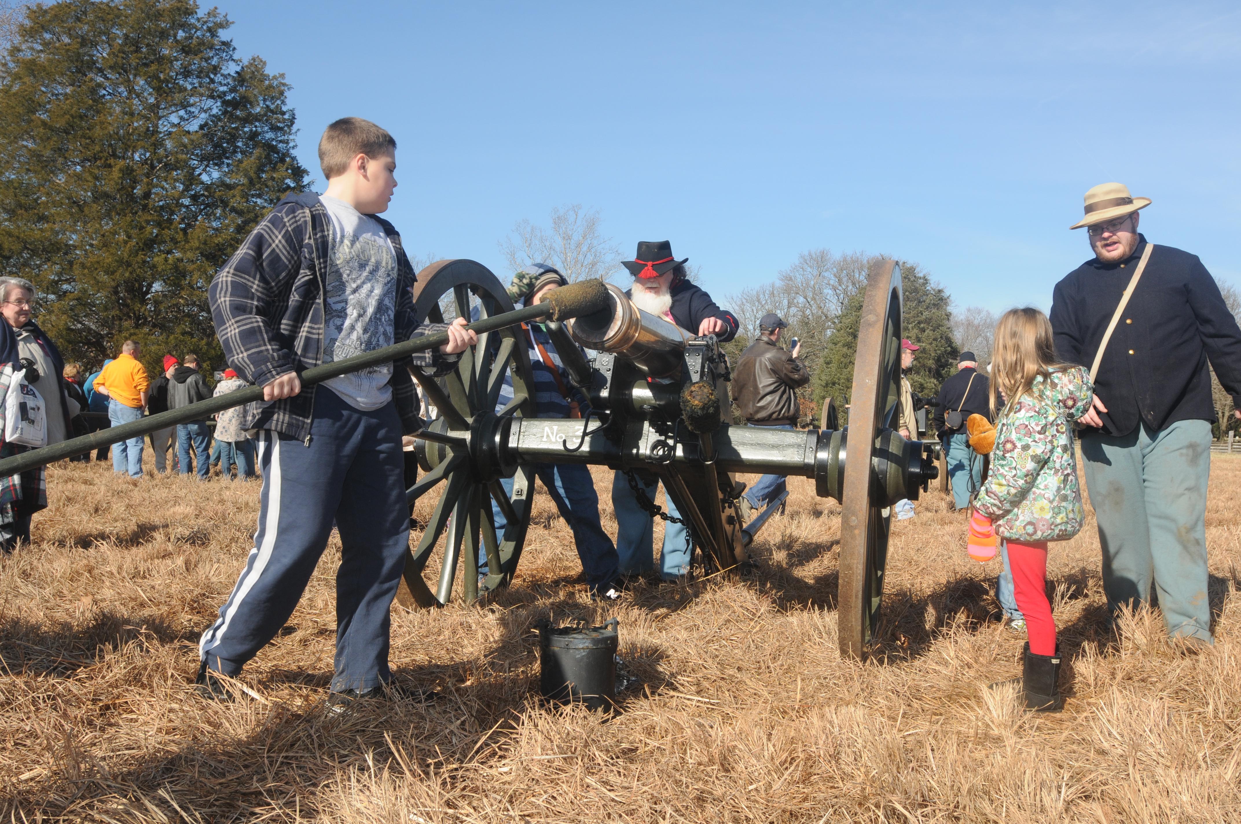 Young people perform the drill to load a cannon under the direction of volunteers.