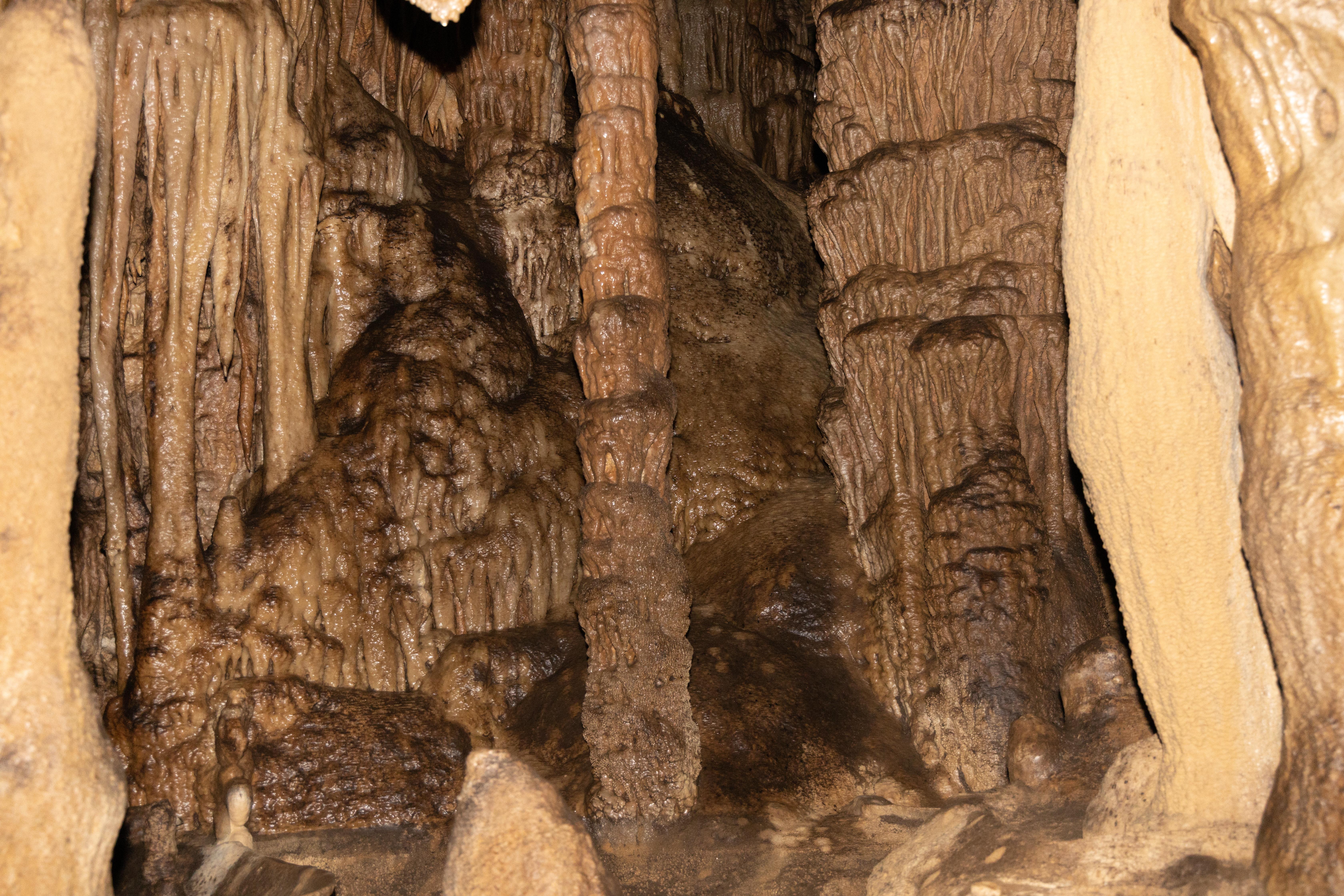 Rock formations cling to the ceiling and walls of a cave passageway.