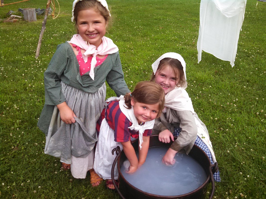 three young girls in historical clothing tending to laundry