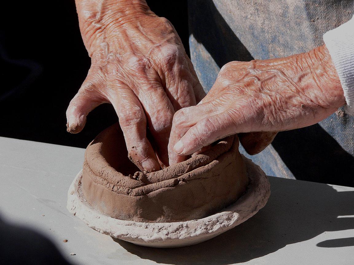 A pair of hands works to shape a brown colored clay into the base of a traditional, handmade pot.