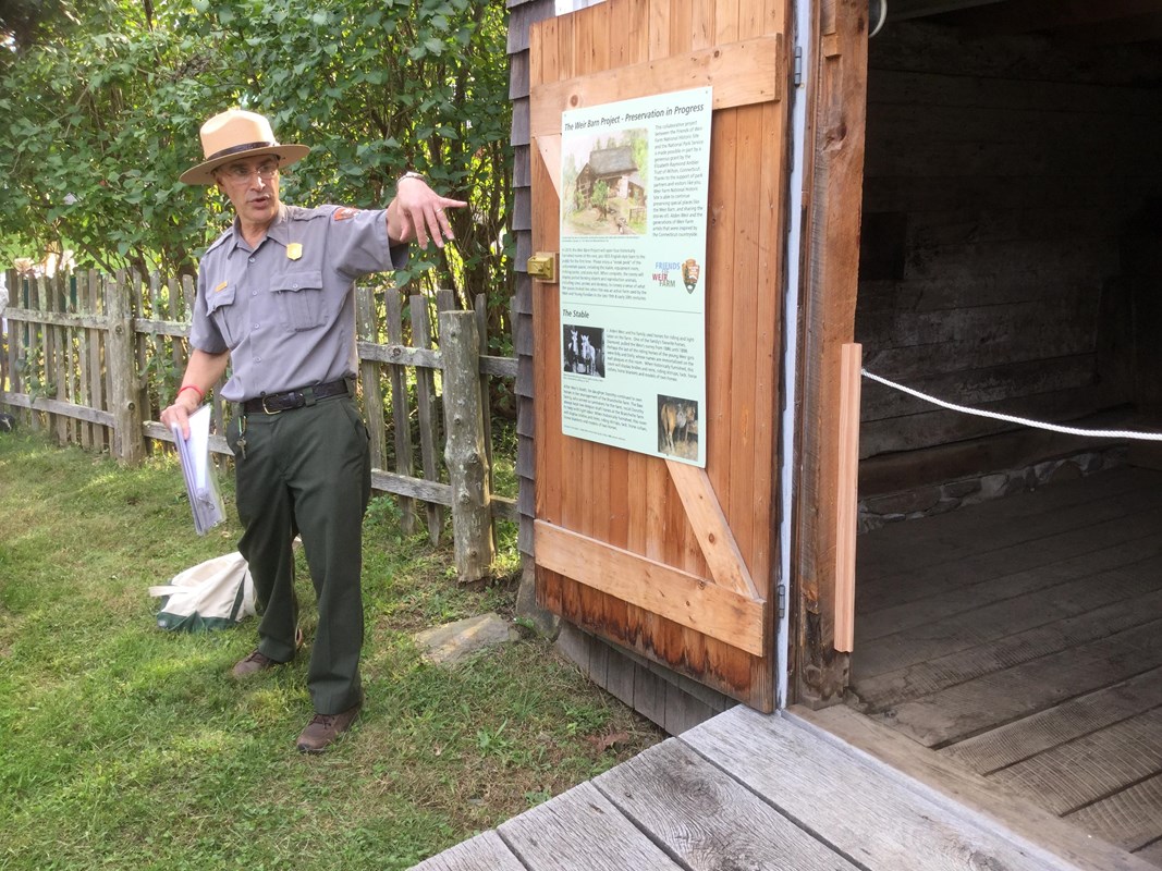 A ranger points to an open barn door while on a tour.