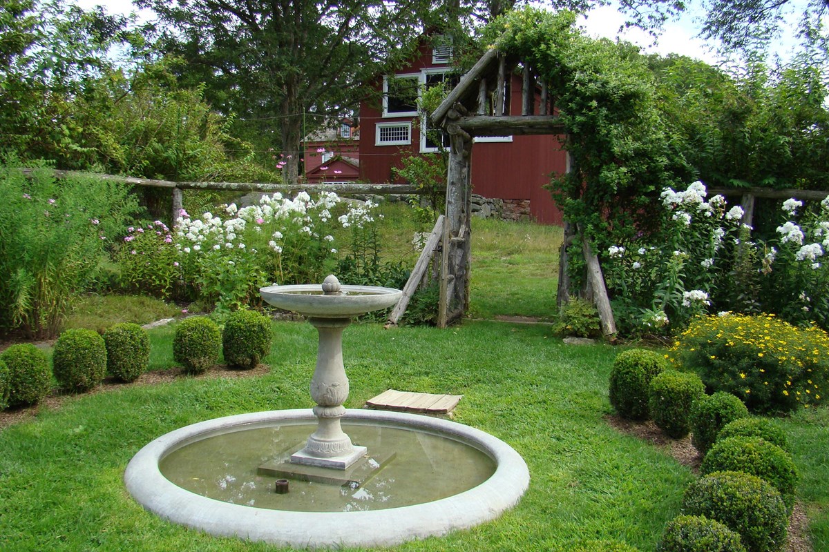 A fountain in a garden with several shrubs and flowers surrounding it.