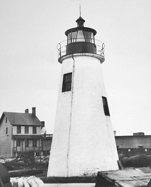 Tall, conical lighthouse stands in front of the lighthouse keepers' house.