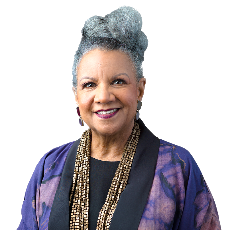 A well-dressed woman wears a white headband, earrings, & pearl necklace in front of gold background