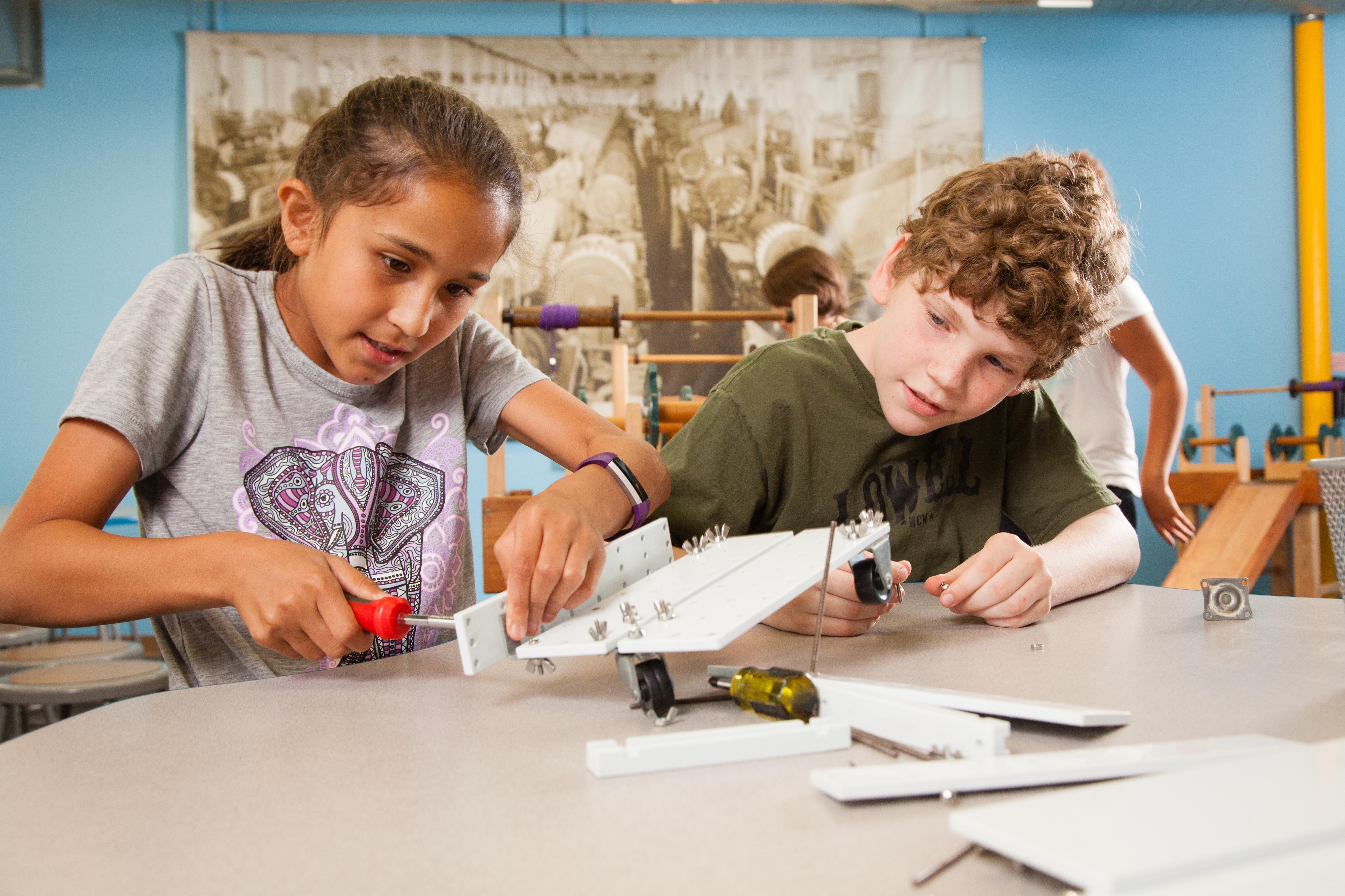 Two children work together to screw together machine parts.