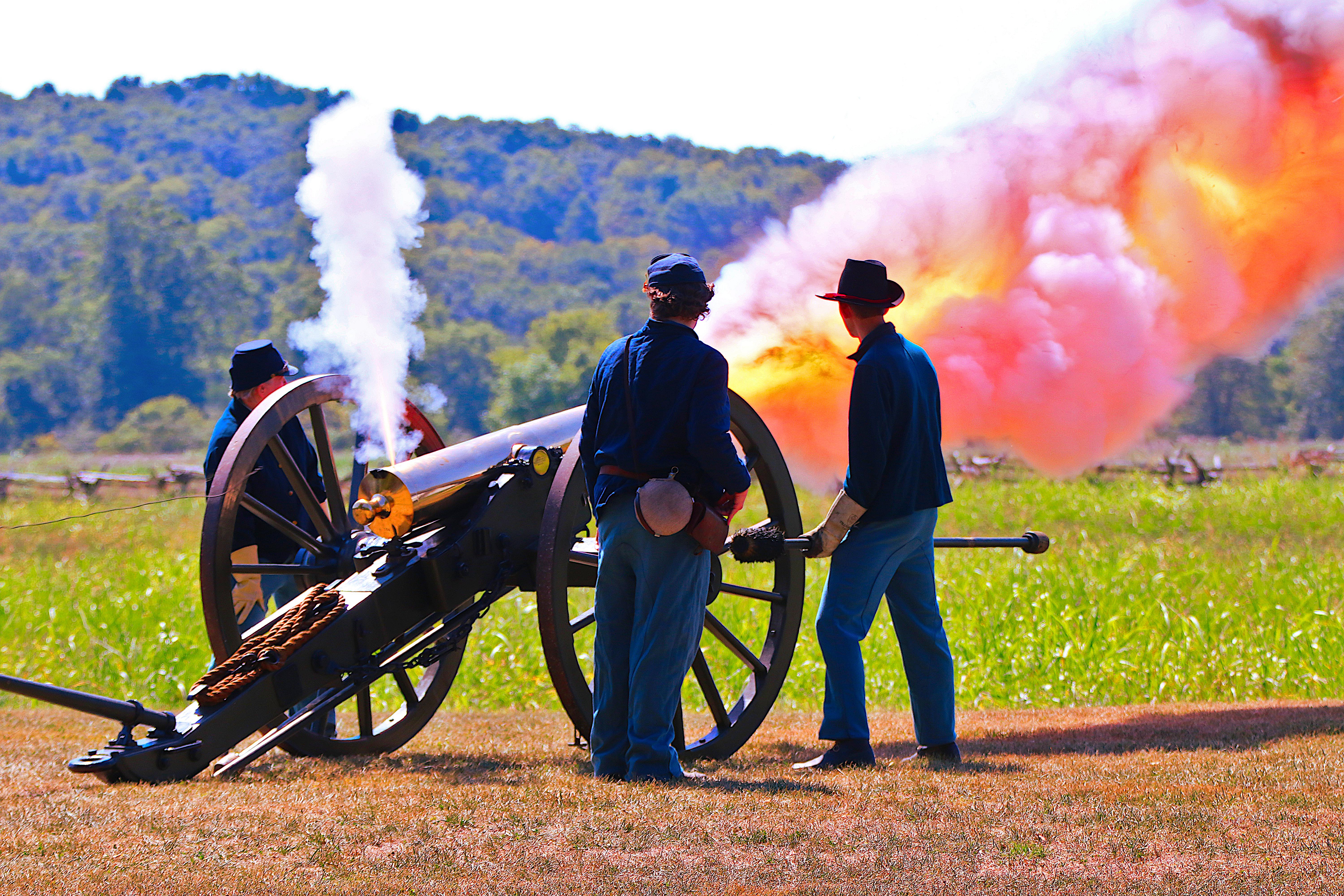 Three people in Civil War uniforms fire a round from a cannon