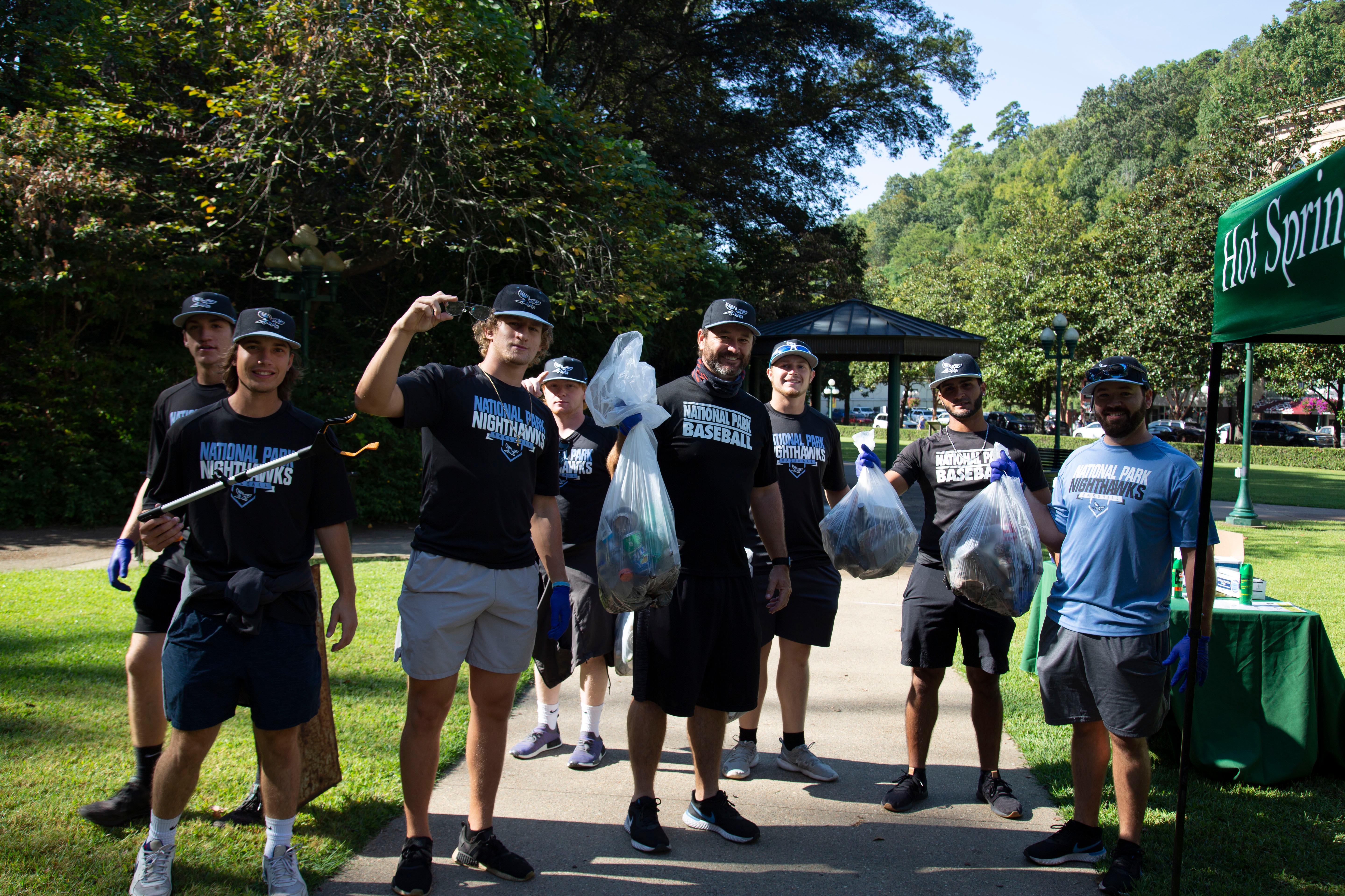 A group of volunteers in matching t-shirts pose with full trash bags and trash grabbers.