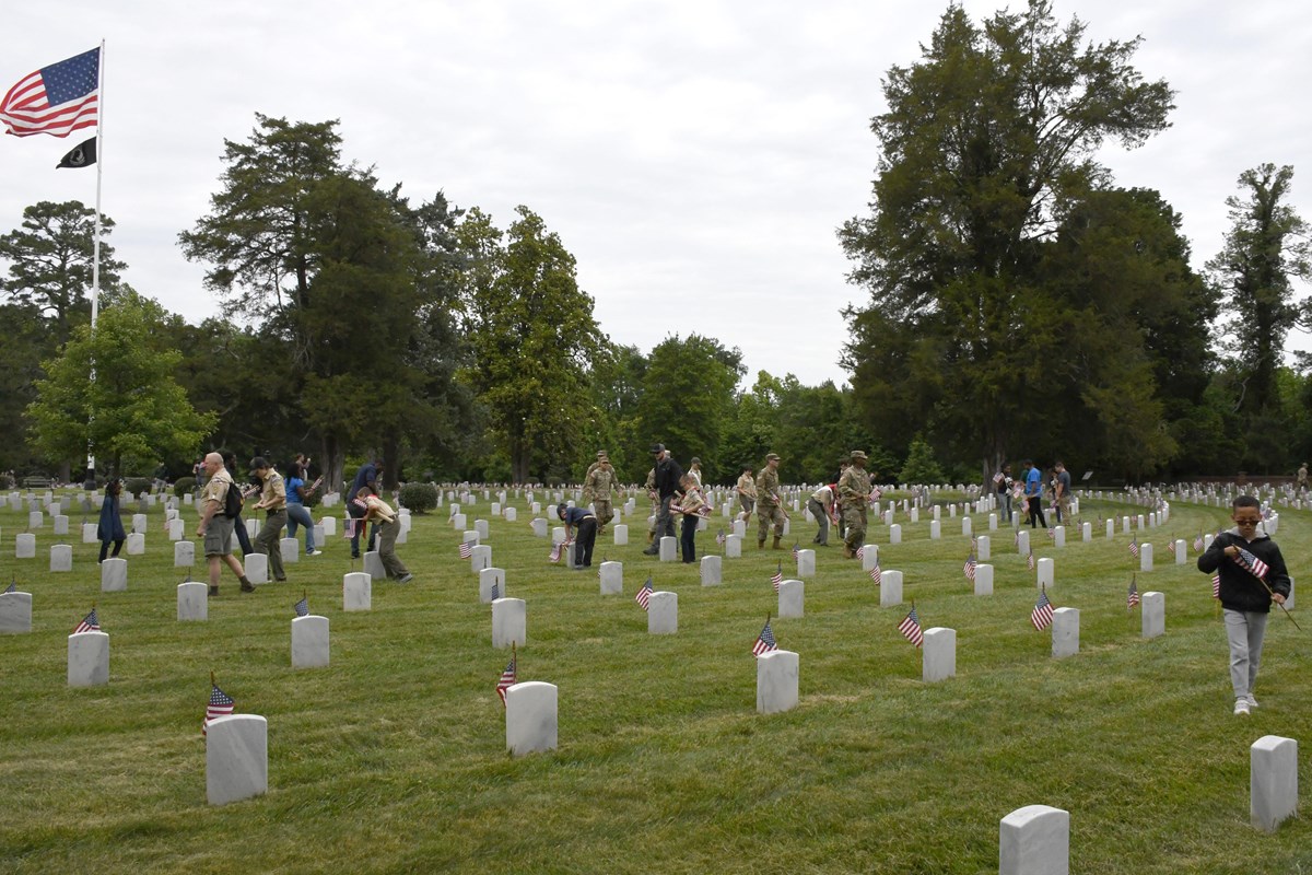 A group of scouts carrying small U.S.A. flags in a cemetery.