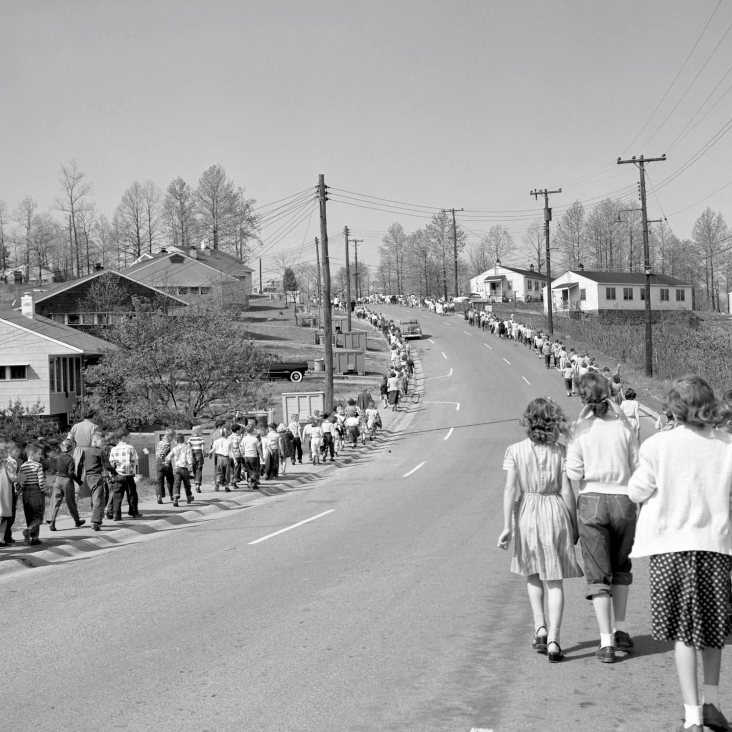 Students walk on either side of a residential street up a hill.