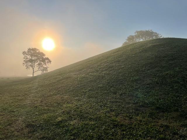 The sun rises behind a large earthen mound.