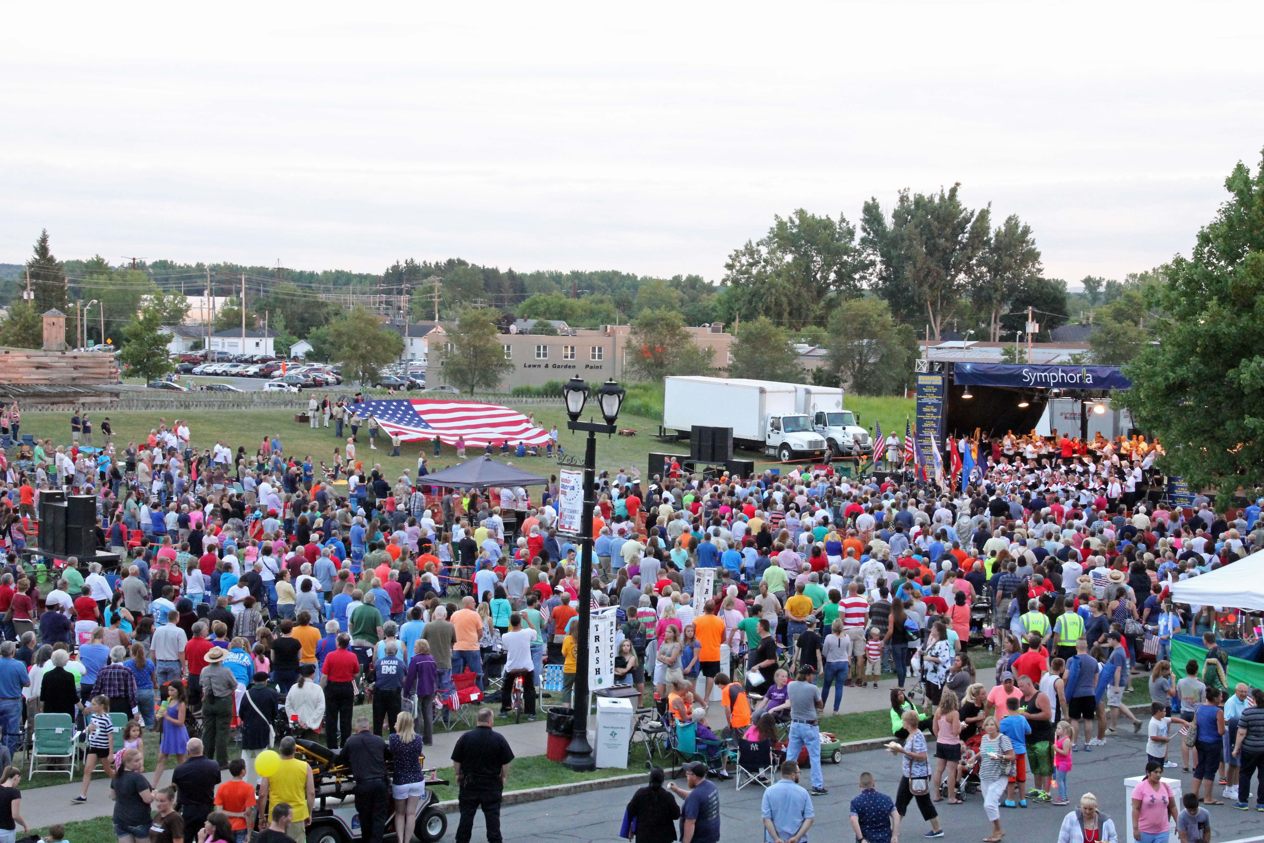 A large flag held by about 30 people on a grassy hill. A crowd stands nearby watching.