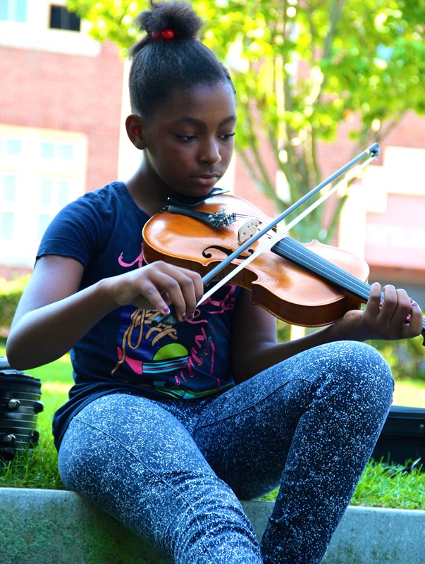 A girl and a man play the fiddle together in the park