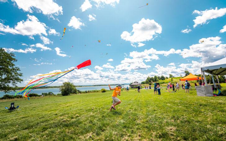 Kid running across a field waving a kite behind them. Other families with kites in the background.