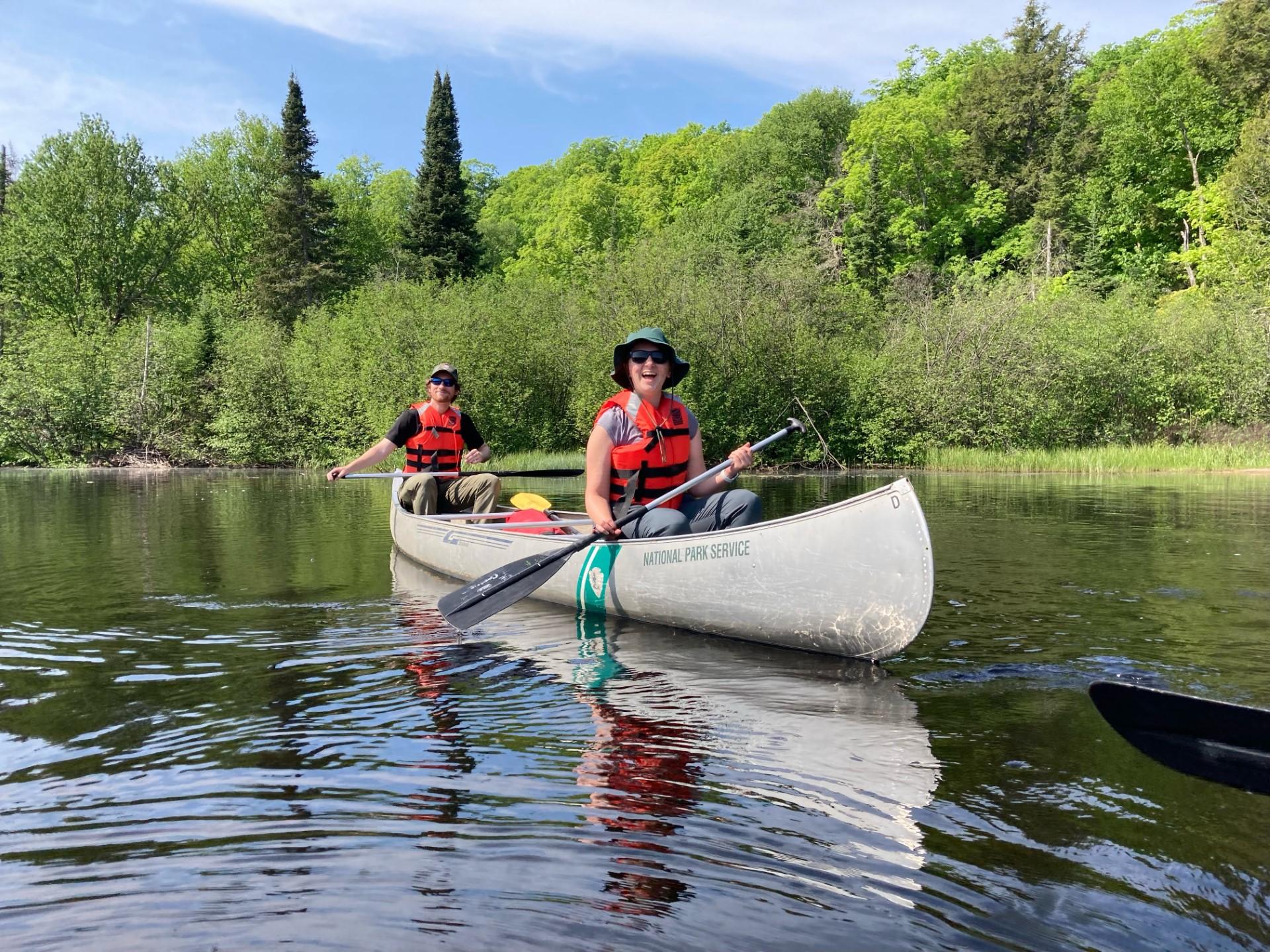 Two people wearing life jackets in a metal canoe smile at the camera.