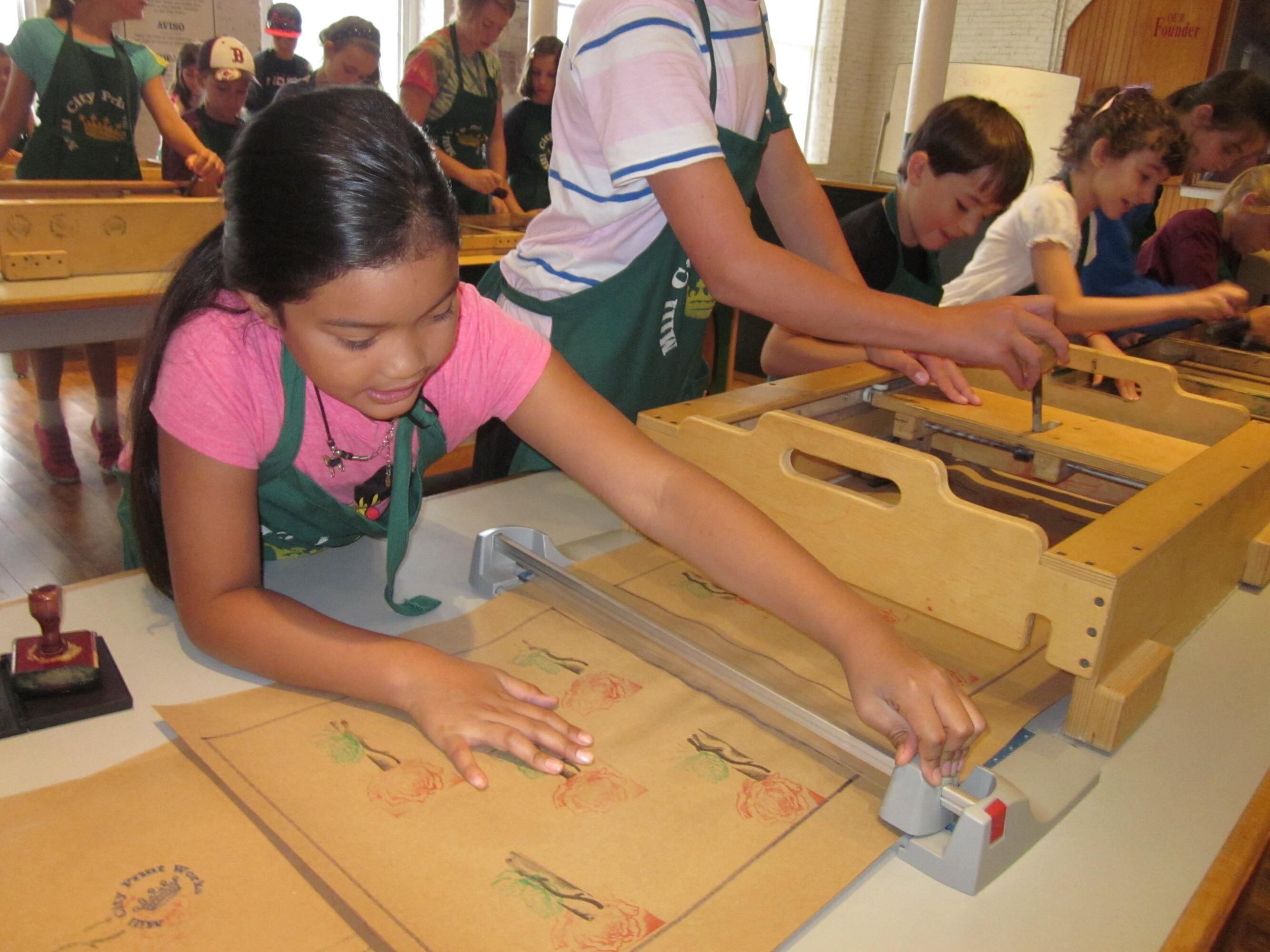 A child works to cut a piece of paper at the end of an assembly line