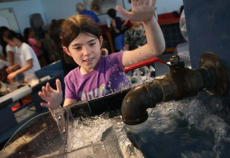 A child looks on as a spigot shoots out water