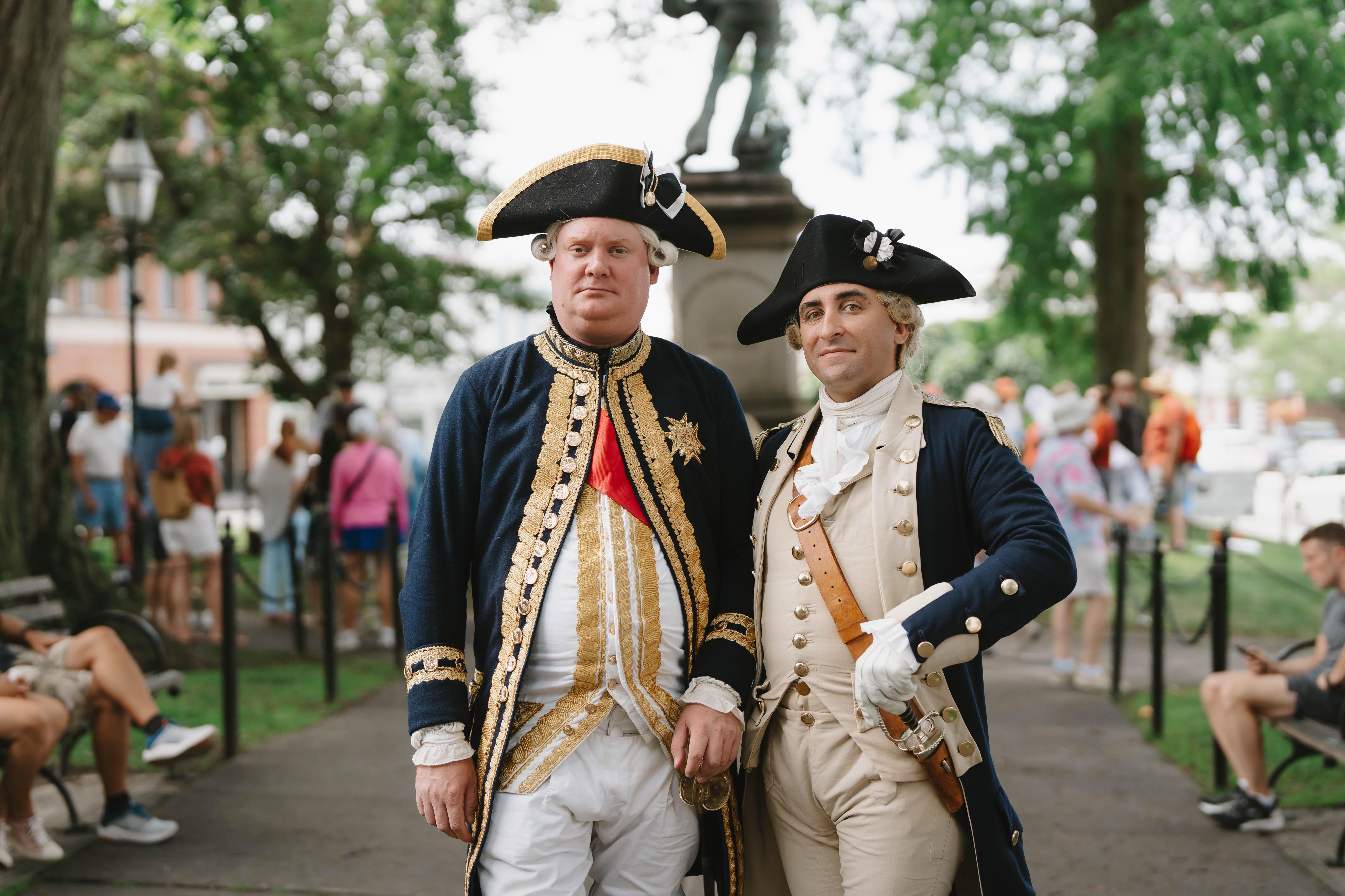 Two Revolutionary War reenactors in French uniforms stand in Washington Square