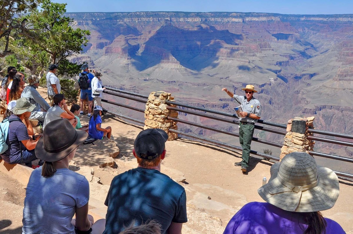 At a scenic overlook with railings, a park ranger is presenting a talk to a group of park visitors.