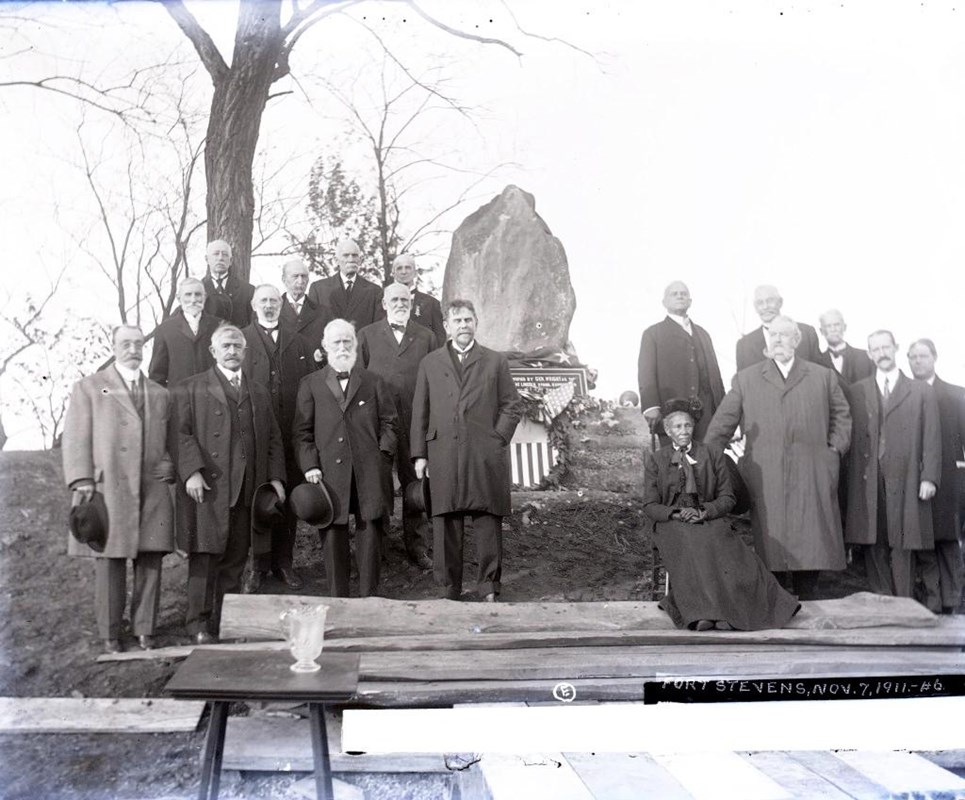 Black and White image of people standing by a stone boulder at Fort Stevens