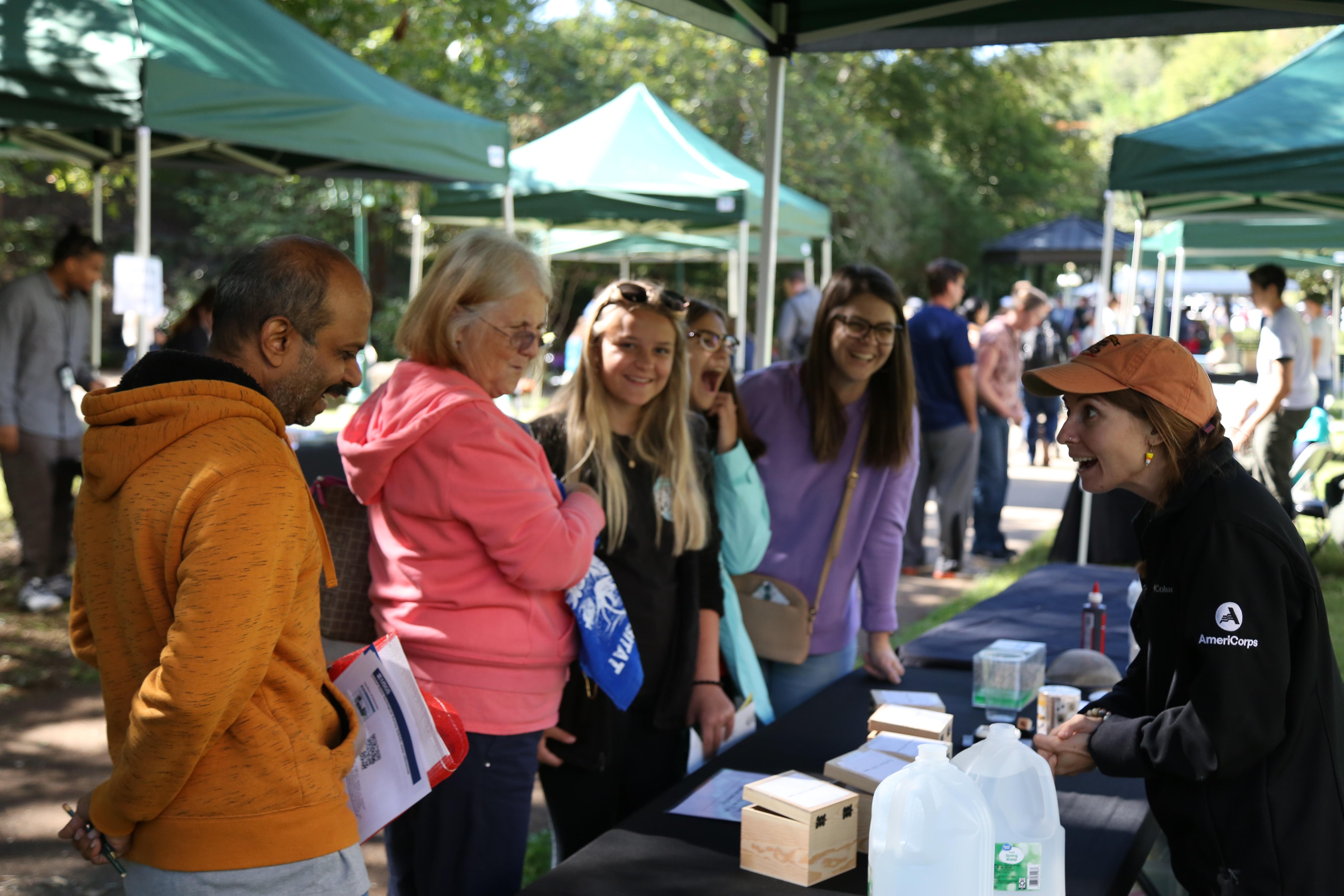 A uniformed ranger speaks to a group of smiling visitors at an outdoor festival