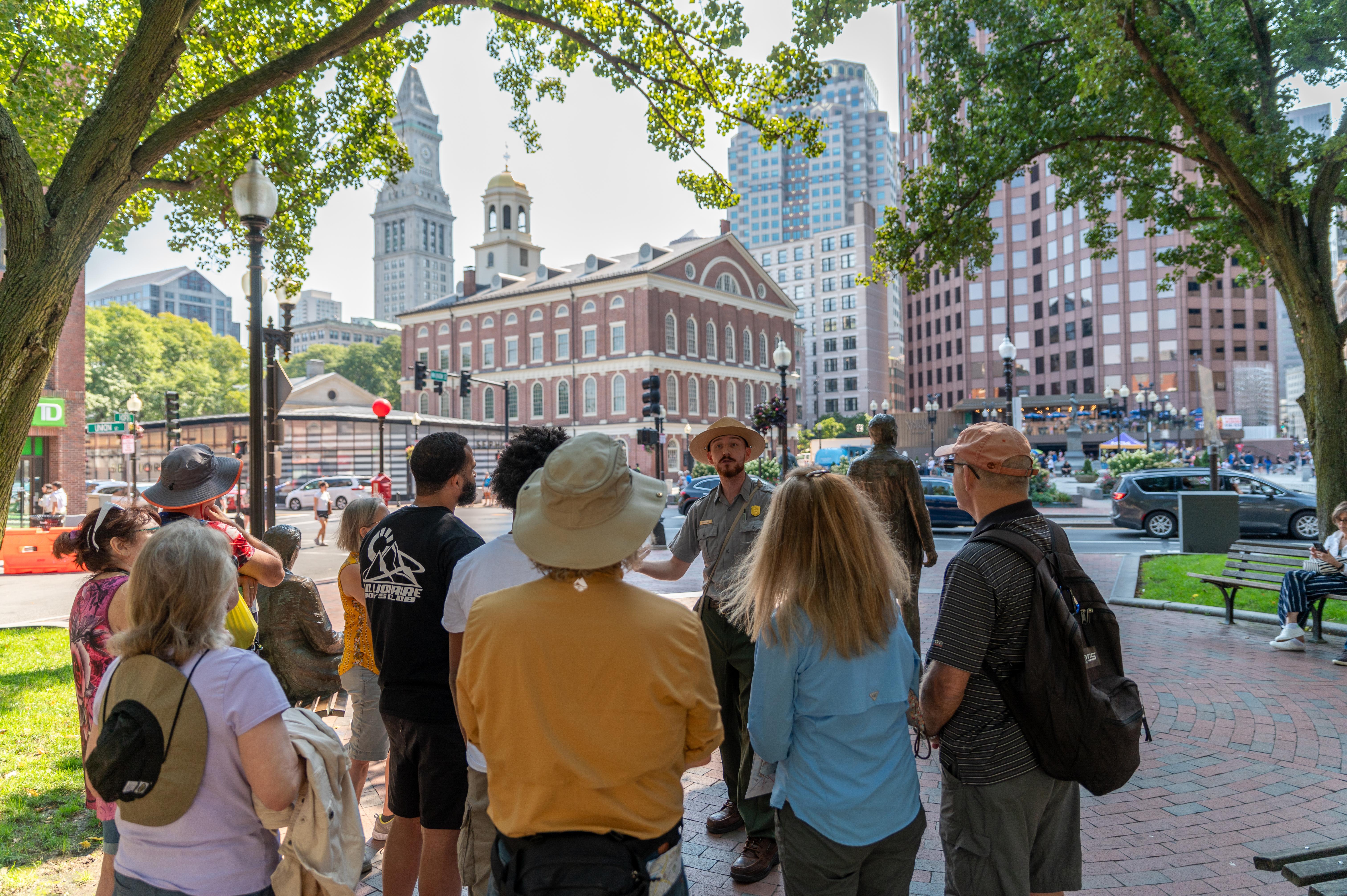 Visitors stand in front of a Ranger leading a tour, Faneuil Hall is in the background