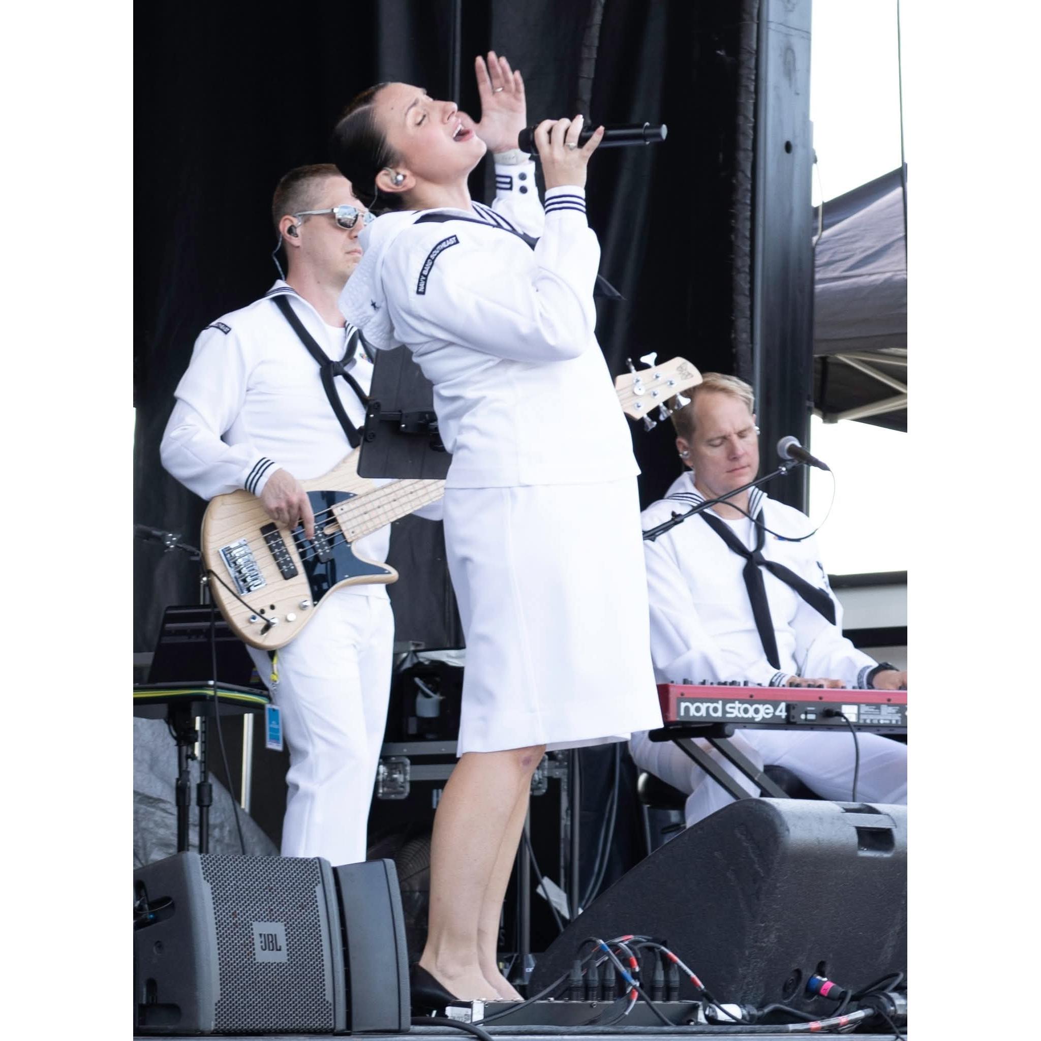 Three sailors in their dress white uniforms playing guitar, keyboards, and singing