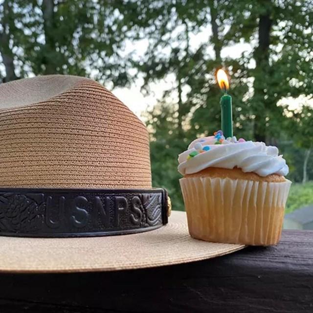 A cupcake with a lit birthday candle sitting on a park ranger hat