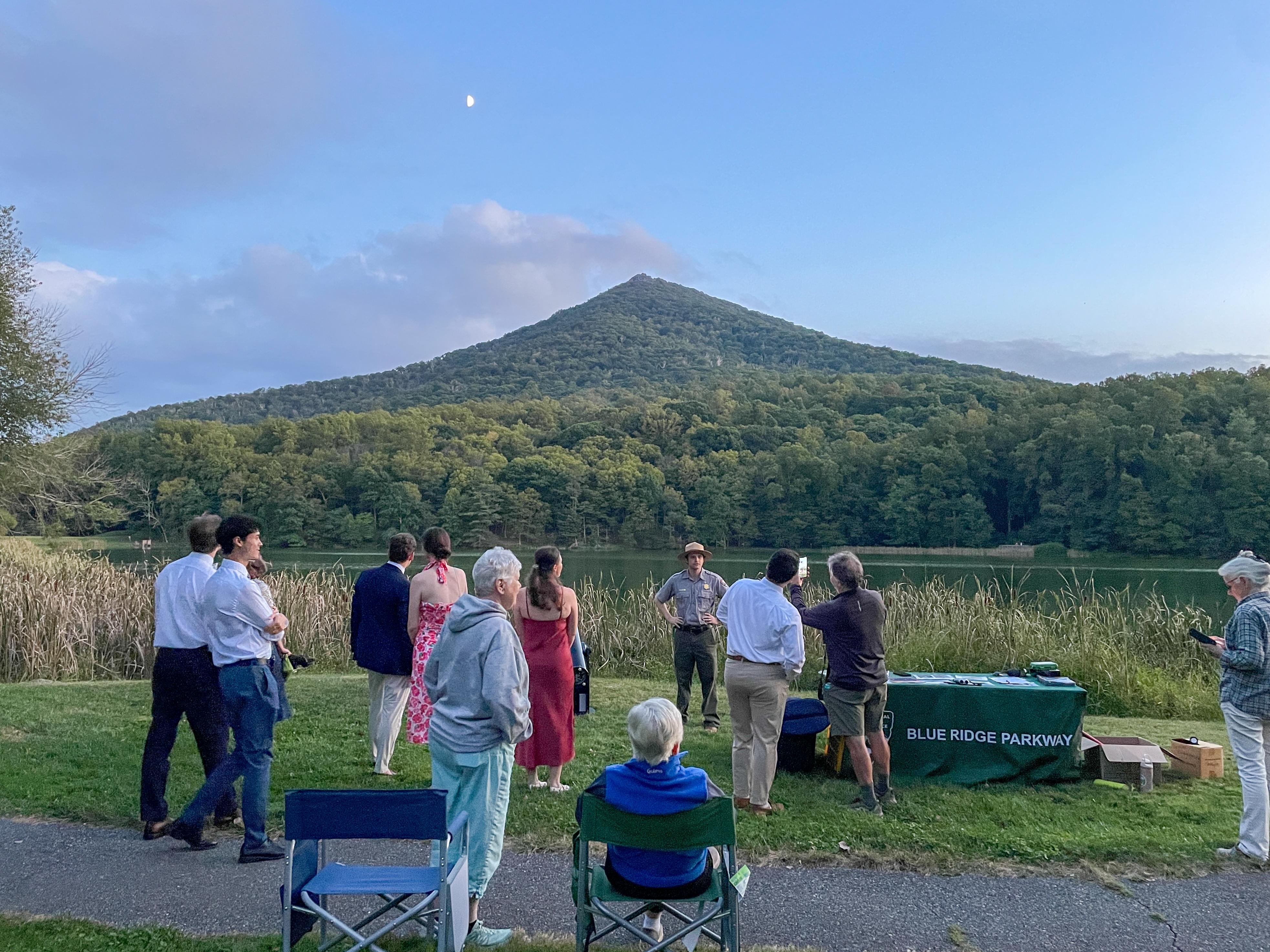 10 people stand around a uniformed ranger looking at the night sky with a mountain in the background