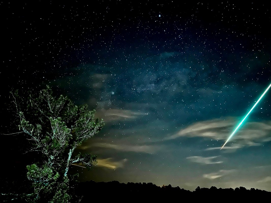 A fireball streaking across the night sky viewed from a high overlook